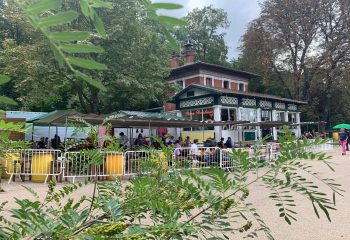 Rosa Bonheur: Outdoor Parisian cafe scene. People at tables, greenery, and architecture. Popular gay-friendly spot for drinks and socializing.