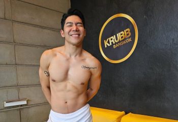 Shirtless man smiling in front of the Krubb Bangkok logo. Gay travel in Bangkok. Krubb is a gay sauna in Bangkok.