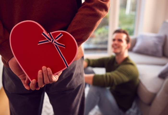 Gay couple: Man holding heart-shaped gift behind back for partner. Top gift ideas for male partners. 700X480-1.jpg.