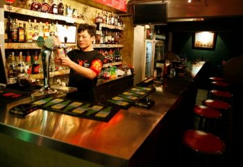 Kai Club barman pouring beer. Gay travel advice for men. Nightlife at 700X480-5.jpg. Bar with stools, bottles, and TV.