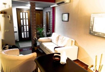 Adoneys Gay Massage in Madrid: Interior view of a massage room with a white sofa, massage table, and decorative elements.