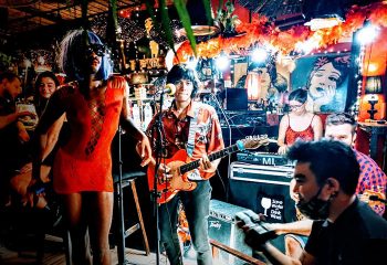 Alcove Koh Phangan beachfront bar: Live music performance at a gay-friendly venue. A drag queen in a red dress stands next to the band.