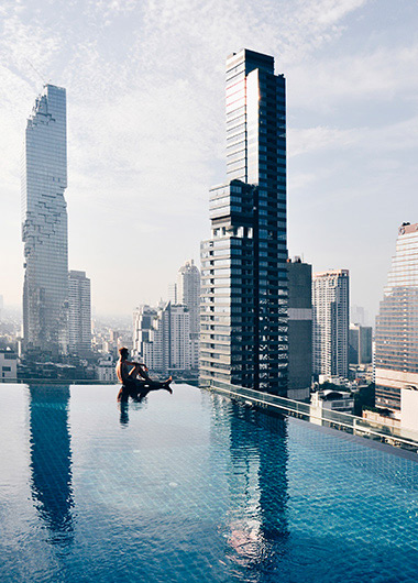 Gay travel: Man at Amara Bangkok rooftop pool in Silom, a popular gay spot. The infinity pool offers stunning city views, a must-visit.