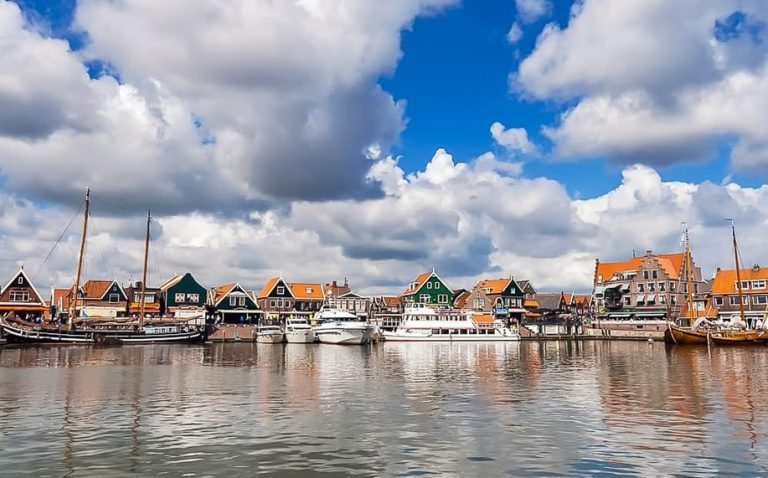 Amsterdam's Dutch Countryside tour: Waterfront view with boats, traditional houses, and a cloudy sky. Perfect for gay travel advice.