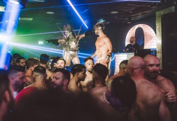Aqua Club, a gay cruise club in Torremolinos, Spain. Party scene with shirtless men and performers in costumes under blue and green lights.