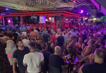 Crowded Aqua Club, a gay cruise club in Torremolinos. Many gay men are socializing in the bar, under bright lights. Gay travel advice.