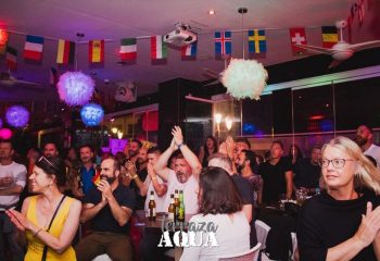 Aqua Club gay cruise club in Torremolinos. Cheering crowd at Terrazza Aqua, a popular gay bar. Flags and festive lights decorate the space.
