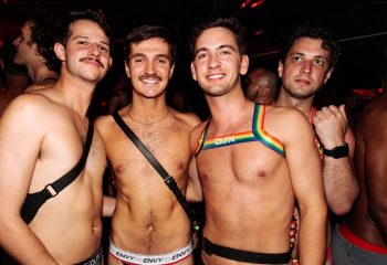 Arq Sydney: Group of shirtless gay men at a party, some wearing harnesses and underwear, smiling at the camera. Gay travel advice.