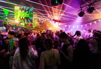 Arq Sydney: Gay men dance at a vibrant nightclub with laser lights and colorful decorations. Energetic nightlife scene for LGBTQ+ travel guide.