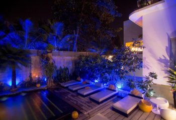 Arthur & Paul men-only hotel pool area at night. Gay travel destination with blue lighting, lounge chairs, and tropical plants. Relaxing vibe.