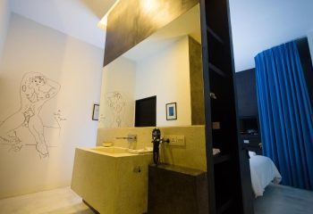 Arthur & Paul men-only hotel bathroom. Modern design with a sink, mirror, and a drawing of a nude man on the wall. Gay travel.