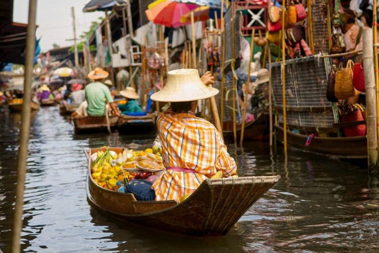 Bangkok Floating Markets scene. Person in boat sells fruit. Gay men travel to Thailand for cultural experiences like classical bicycle tours.