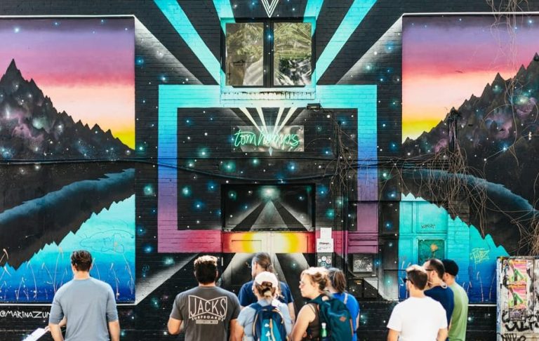 Berlin Street Art Walking Tour: Vibrant mural with mountains and neon sign. Group of people exploring the wild art scene. Gay travel.