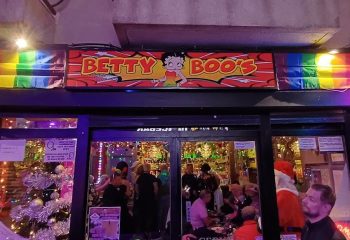Betty Boo's Gay Bar in Benidorm. Entrance view with people inside, rainbow flag, and Christmas decorations. Gay travel advice.