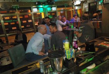 Betty Boo's gay bar in Benidorm. Men socializing at the bar, rainbow flag in the background. Gay travel destination, nightlife.