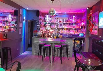 Interior of Betty Boo's gay bar in Benidorm, Spain. Disco ball, bar stools, and shelves of liquor bottles under colorful lighting.