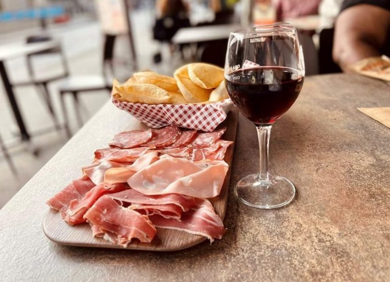 Milan street food tour: Cured meats and bread on a wooden board with a glass of red wine. Enjoy local flavor on a gay-friendly tour.