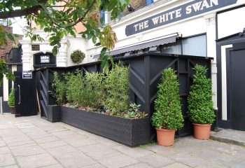 BJ's White Swan Gay Club, London. Exterior view of the pub with black fencing and greenery, popular gay travel destination.