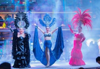Blue Chilli Phnom Penh show. Three drag queens in colorful, feathered costumes perform on stage. Gay travel in Cambodia.