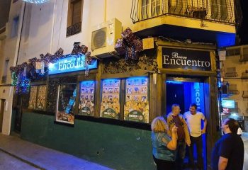Brief Encuentro gay bar in Benidorm. Exterior view at night with people standing outside. Gay travel destination, nightlife scene.