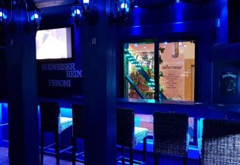 Interior of Brief Encounter Gay Bar in Benidorm. Blue lighting, bar stools, drinks menu, and TV screen. Gay travel nightlife.