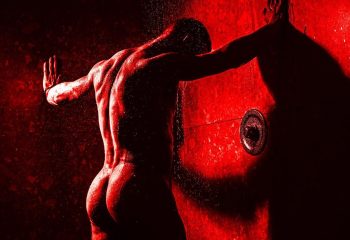 Red-toned image of a muscular, nude man in a shower at Bunker Bar, Sydney. Gay men's travel destination. Sensual, artistic.