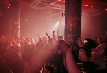 Burdekin Hotel Sydney: Gay men dancing at a party in a smoky, red-lit club. People are cheering with hands raised. Nightlife scene.