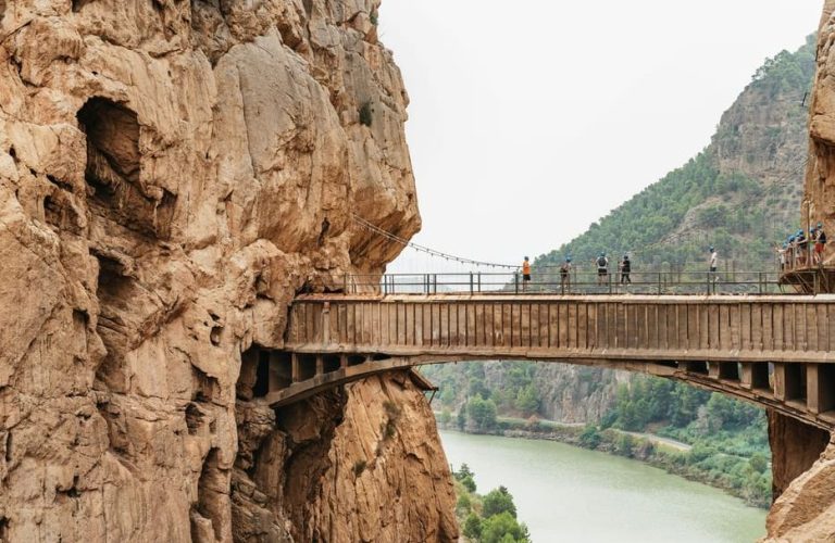 Caminito del Rey hike, Spain. Chic adventurers on a high bridge between cliffs. Epic gay travel destination from Torremolinos.