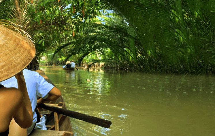 Mekong Delta escape: Boat trip in Ben Tre, Vietnam. Gay-friendly travel. Lush green scenery, tranquil river, and traditional conical hat.