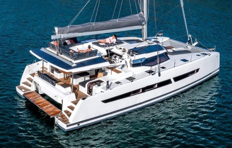 Luxury catamaran cruise. Gay travel: Two men relaxing on a white catamaran with sails in blue water. Chill in style with a 3-course feast.