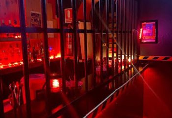 Inside Copper Private Club, a gay cruising bar in Benidorm. Red lighting illuminates the bar area behind metal bars, creating a sensual atmosphere.