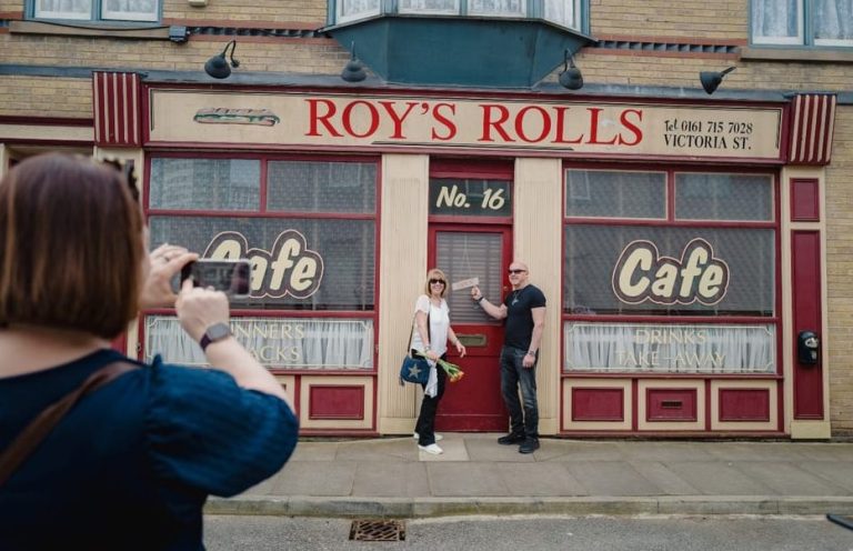 Coronation Street Tour: Roy's Rolls cafe. Tourists pose outside the iconic Manchester TV set. Gay travel destination. Walk the cobbles!