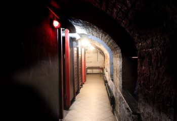 CoxxMen's Bar, Budapest. Dark, arched corridor with red-trimmed doors. Gay travel destination for men.