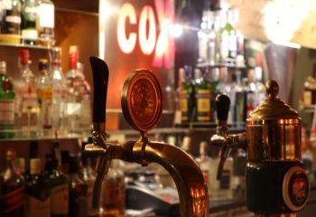 Coxx Men's Bar interior, Budapest. Beer taps and bottles on shelves. Gay travel advice. Nightlife scene, bar setting.