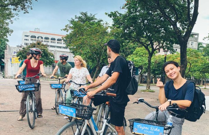 Gay-friendly Taipei bike tour. Group of tourists on bicycles with baskets, exploring Taipei. Morning tour with breakfast, city vibes.