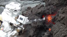 A person in a protective suit sticks a long measuring device directly into a lava flow