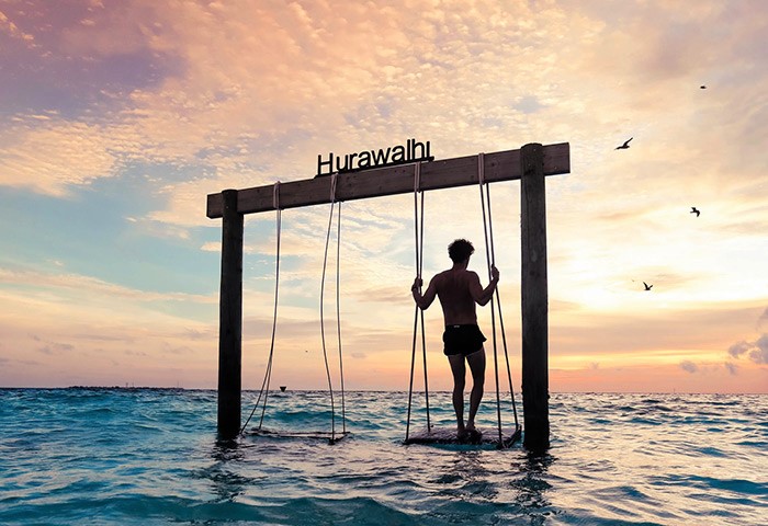 Gay travel: Man on swing in the Maldives at sunset. Hurawalhi island experience. Is it safe for LGBTQ+ travellers to visit? Local island experiences.