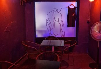 Interior of Eagle Bar, a gay bar in Torremolinos. Features tables, chairs, and a drawing of a man's back on a wall.