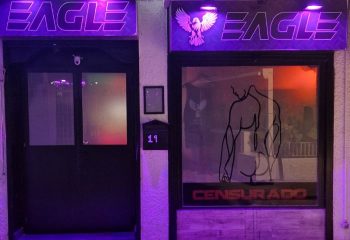 Eagle Bar, a gay bar in Torremolinos, Spain. Neon signage, censored image of a man's physique in the window. Gay travel destination.