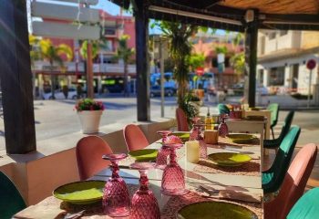 El Gato Lounge gay bar in Torremolinos: Outdoor dining table set with pink glasses, green plates, and colorful chairs. Gay travel advice.