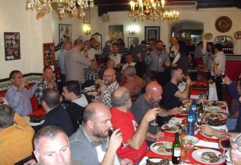 Interior view of El Horno Gay Bar in Sitges, Spain. Many gay men are seated at tables, eating and drinking. Chandeliers hang from the ceiling.