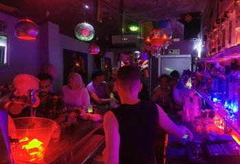Inside Escape Bar, a popular gay nightclub in Benidorm, Spain. Patrons gather at the bar under colorful lights, enjoying the vibrant atmosphere.