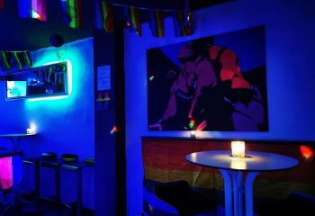 Escape Bar, a gay nightclub in Benidorm. Interior with blue lighting, rainbow flags, and artwork of two men embracing. Nightlife.