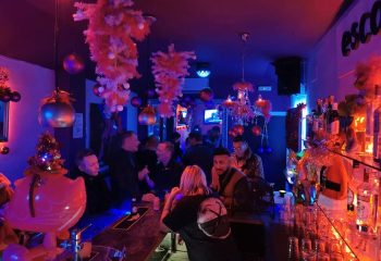 Escape Bar, a gay nightclub in Benidorm. Interior view with patrons at the bar, festive decorations, and blue lighting. Nightlife scene.