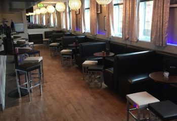Interior of EVA Manchester, a gay bar. Black leather booths, stools, wood floors, and decorative lighting create a stylish atmosphere. Gay travel advice.