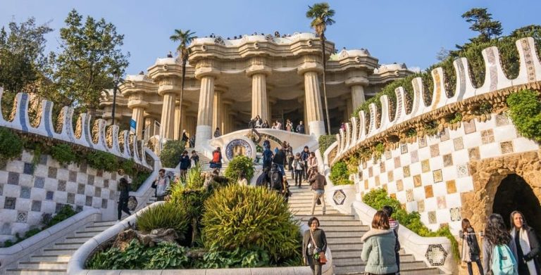 Park Güell, Gaudí's architectural wonderland in Barcelona. Tourists explore the mosaic-covered stairs and colonnaded hall. A gay travel destination.
