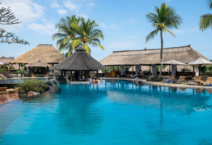 Ubud nightlife: Poolside bar at a gay-friendly resort in Ubud, Bali. Thatched roofs, palm trees, and turquoise water. Gay travel.