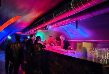 Inside Freud Club Frankfurt: Gay bar with colorful lights, patrons, and bartenders. Gay travel destination.