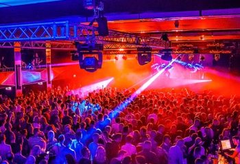 Garcons Budapest event: A large crowd of gay men party under blue & red lights. Stage lighting rig overhead. Budapest gay nightlife.