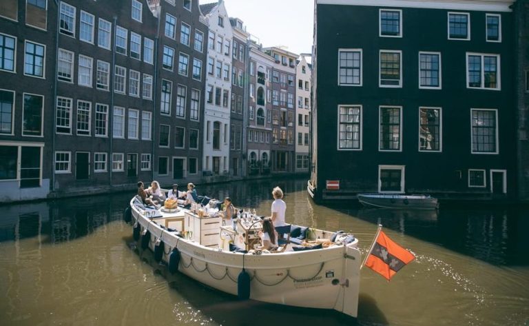Gay-friendly Amsterdam canal cruise. People sip, chill, and snack in style on a boat. Amsterdam's canals and buildings in the background.
